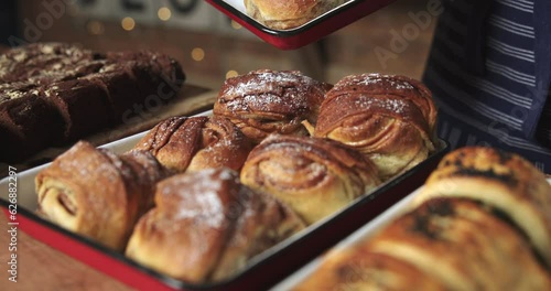 Close Up Of Sales Assistant In Bakery Arranging Display Of Fresh Cinnamon Buns