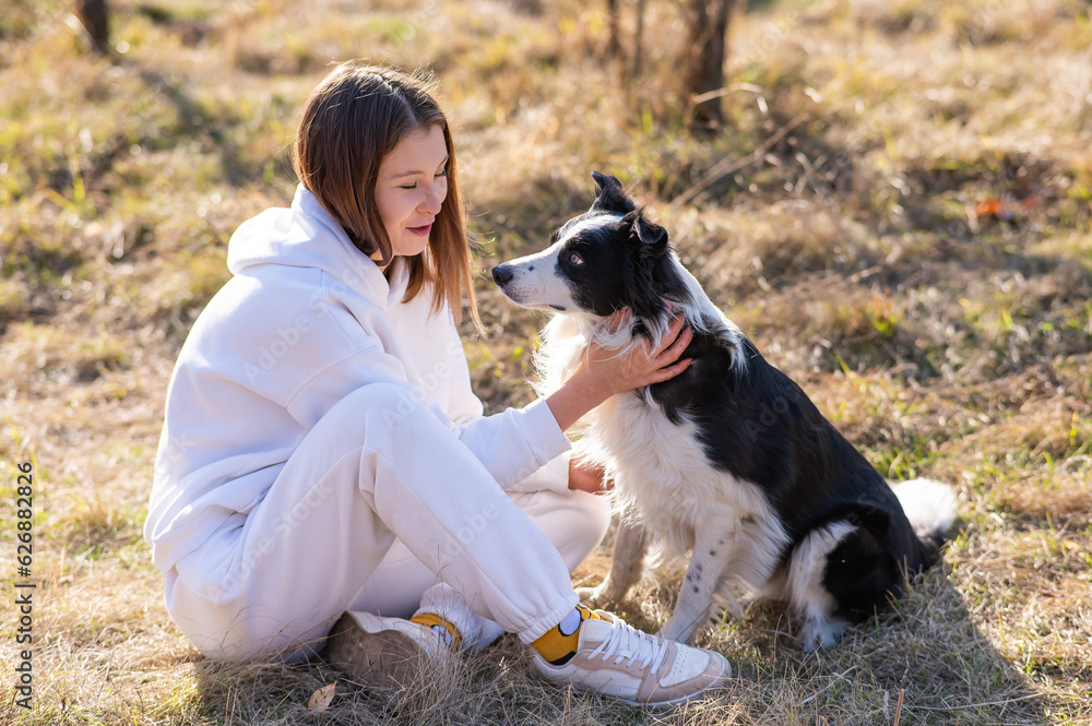 Caucasian woman hugging and kissing her Border Collie dog while sitting on grass in autumn park.