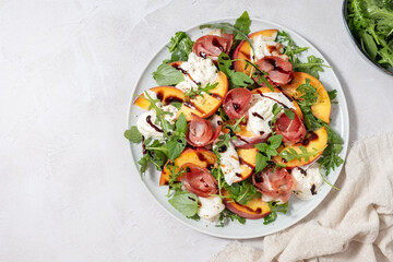 Healthy summer salad with peach, burrata, arugula and jamon