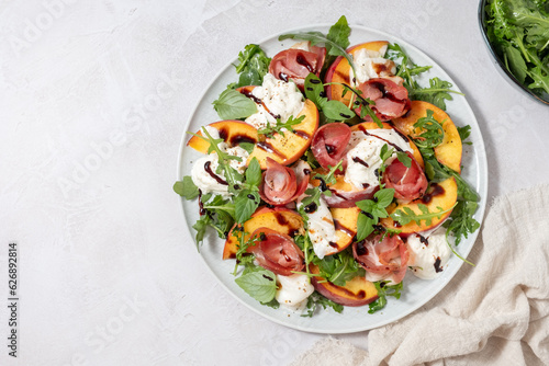 Healthy summer salad with peach, burrata, arugula and jamon