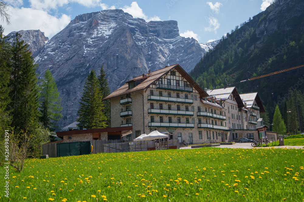 The hotel is located in a valley surrounded by mountains. Small yellow flowers. Nature's Wonderland: Lake Braies and its Captivating Alpine Scenery.