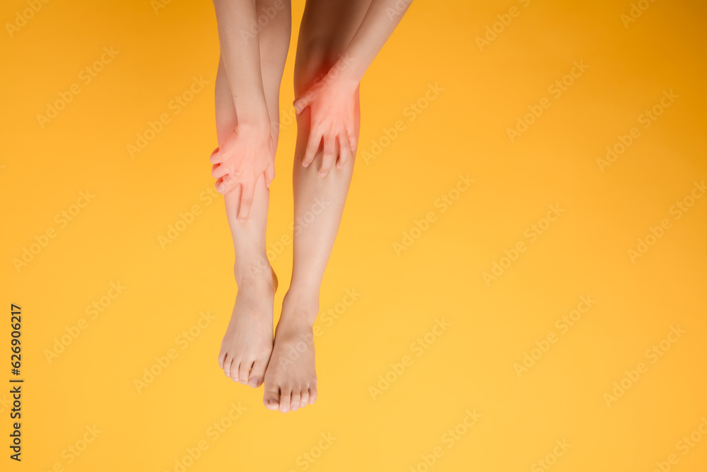 A close up of woman's legs with hands holding their pained legs on a vibrant yellow background. Embodying the concept of legs healthcare. A close up of woman's legs with hands holding their pained legs on a vibrant yellow background. Embodying the concept of legs healthcare.