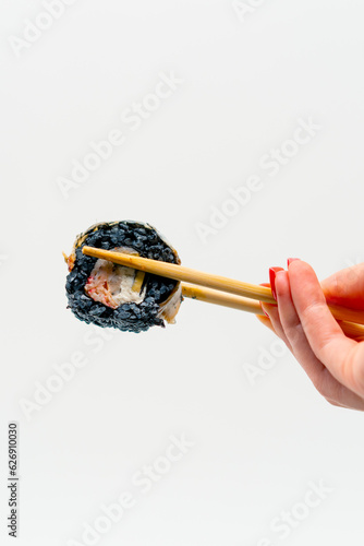 Close-up of sushi california with black rice and eel that a man holds with chopsticks on a white background