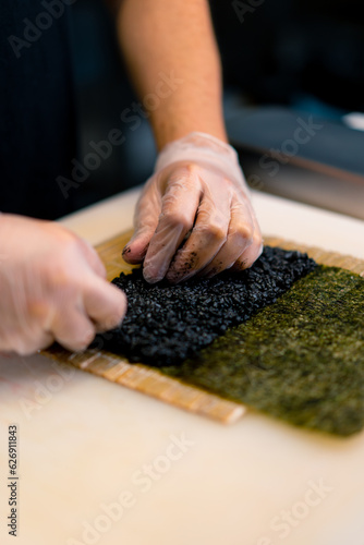 Close-up of a sushi chef spreading black rice on a nori sheet in the process of making rolls in the kitchen of a sushi restaurant