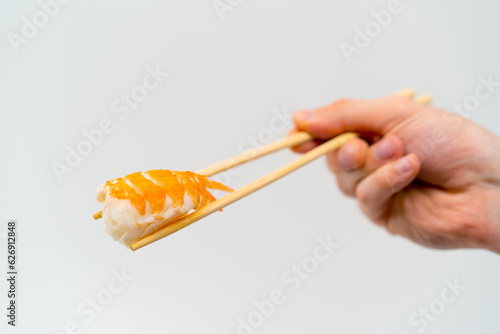 Close-up of a man's hand with chopsticks holding shrimp sushi in the air on a white background