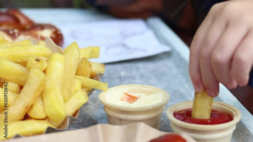 Child's hand dipping french fries in mayonnaise and ketchup close-up Child's hand dipping french fries in mayonnaise and ketchup close-up