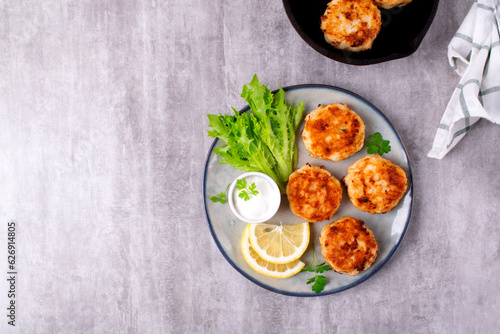 Cutlets with codfish and shrimps served with salad leaves, lemon and sour cream sauce on the plate on gray table. Top view. Copy space