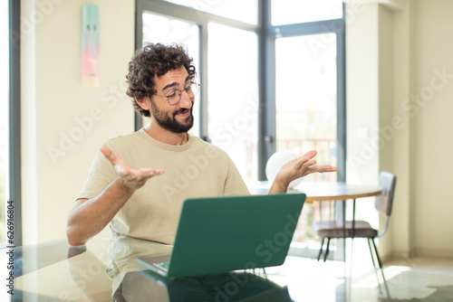 young adult bearded man with a laptop holding an object with both hands on copy space, showing, offering or advertising an object