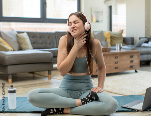 young adult woman practicing yoga feeling ill with a sore throat and flu symptoms, coughing with mouth covered