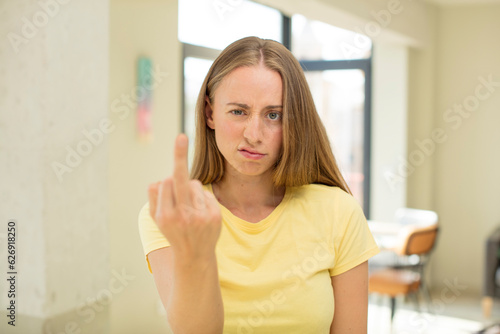 pretty blond woman feeling angry, annoyed, rebellious and aggressive, flipping the middle finger, fighting back