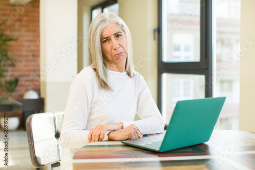 senior pretty woman feeling sad and whiney with an unhappy look and crying with a laptop