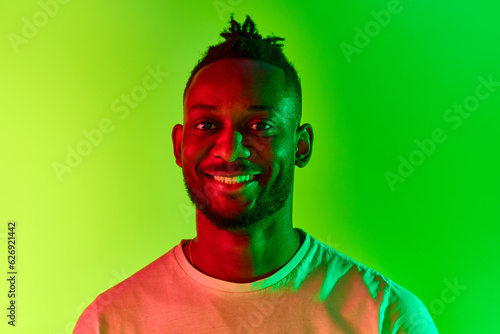 Close up of young african man with dreadlocks looking at camera with smile over gradient yellow-green background in neon. photo