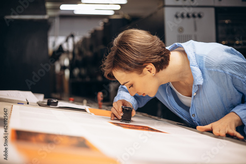 Canvas Print Woman typographer working in printing house with paper and magnifying lens