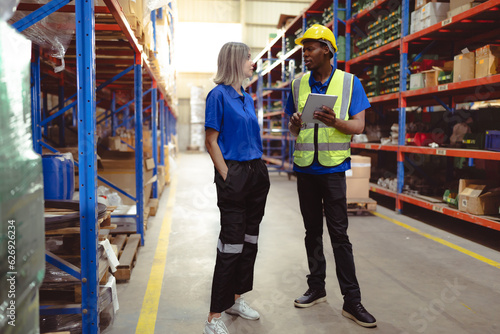 Distribution warehouse manager and client businesswoman using digital tablet checking inventory on shelf. Storehouse supervisor and logistic engineer standing at storage room. Diverse ethnic people.