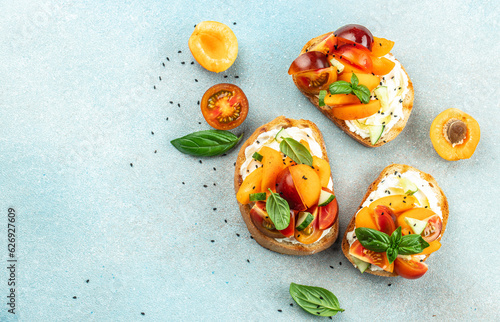 Fototapeta Open sandwiches with cream cheese, peaches, tomatoes and green basil leaves on a light background, Long banner format