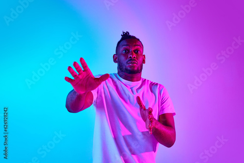 Frightened and withdraw african man looking at camera over colorful studio background in neon.
