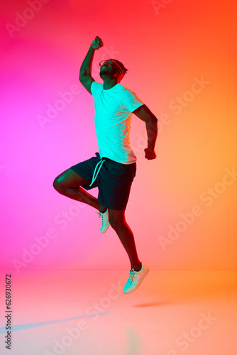 African man in glasses lope happy and laughing over pink-orange background in neon.