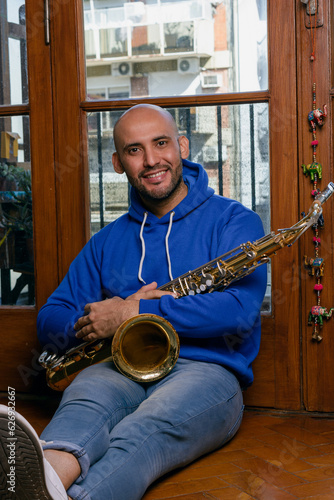 portrait of young latin man saxophonist sitting at home with his saxophone looking at the camera