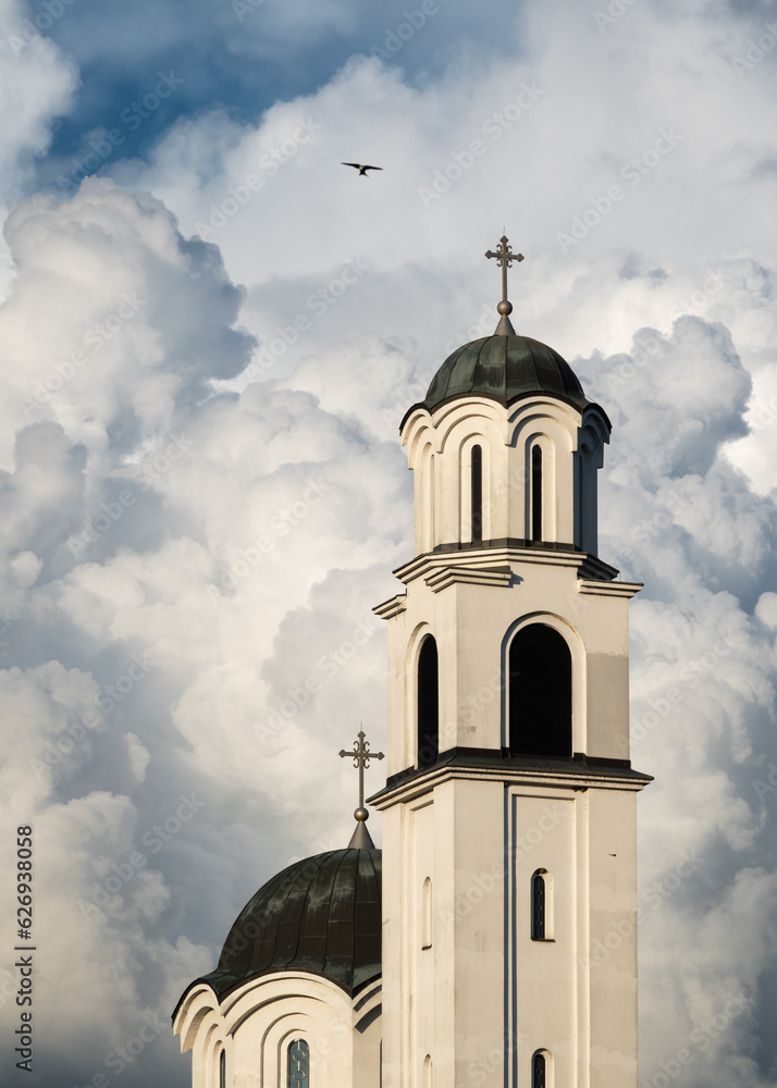 Orthodox church bell tower and pigeon flying next to it against big white cloud, symbol of God and faith