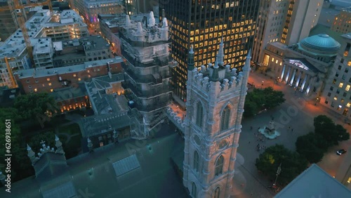 Deep pan up aerial bird eye view shot of Notre Dame basilica in Montreal looking down on the roof and towers in front of Place Jacque Cartier square surrounded by big buildings photo