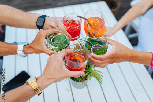 Fotografie Group of friends toasting multicolored cocktails at the summer terrace