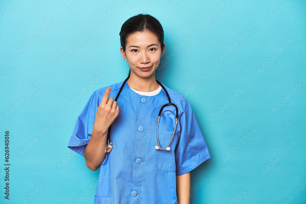 Asian nurse with stethoscope, medical studio shot, pointing with finger at you as if inviting come closer.