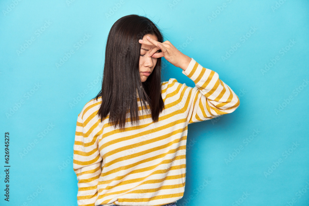 Asian woman in striped yellow sweater, having a head ache, touching front of the face. Asian woman in striped yellow sweater, having a head ache, touching front of the face.