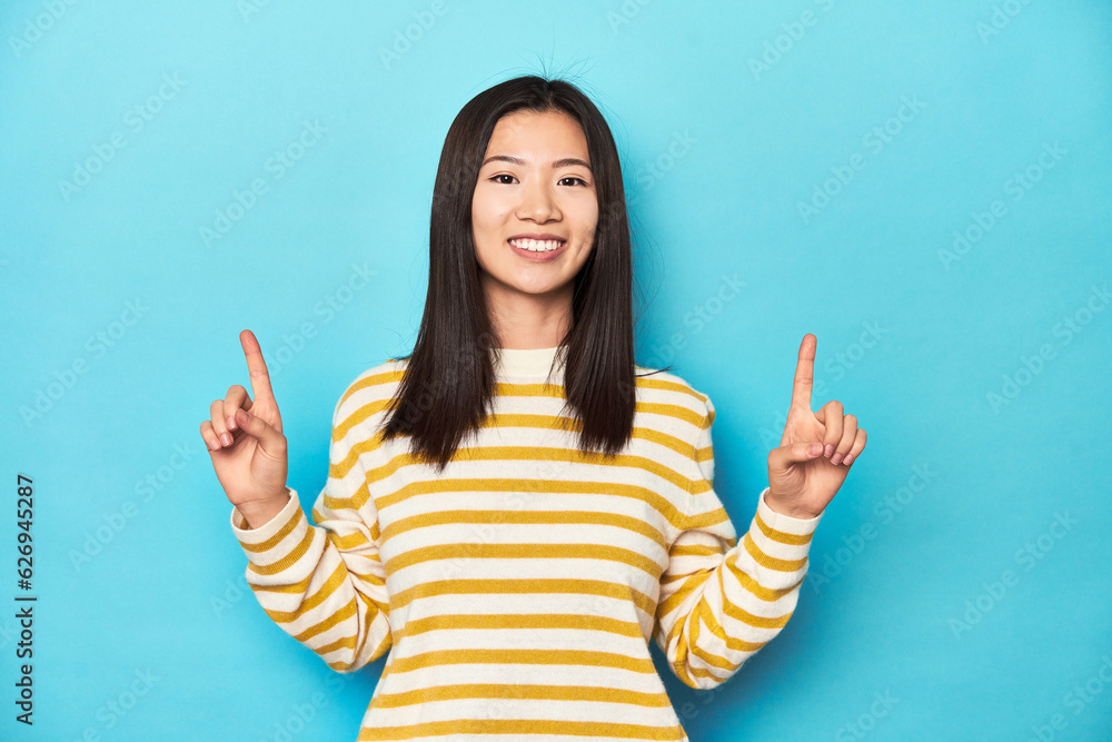Asian woman in striped yellow sweater, indicates with both fore fingers up showing a blank space. Asian woman in striped yellow sweater, indicates with both fore fingers up showing a blank space.