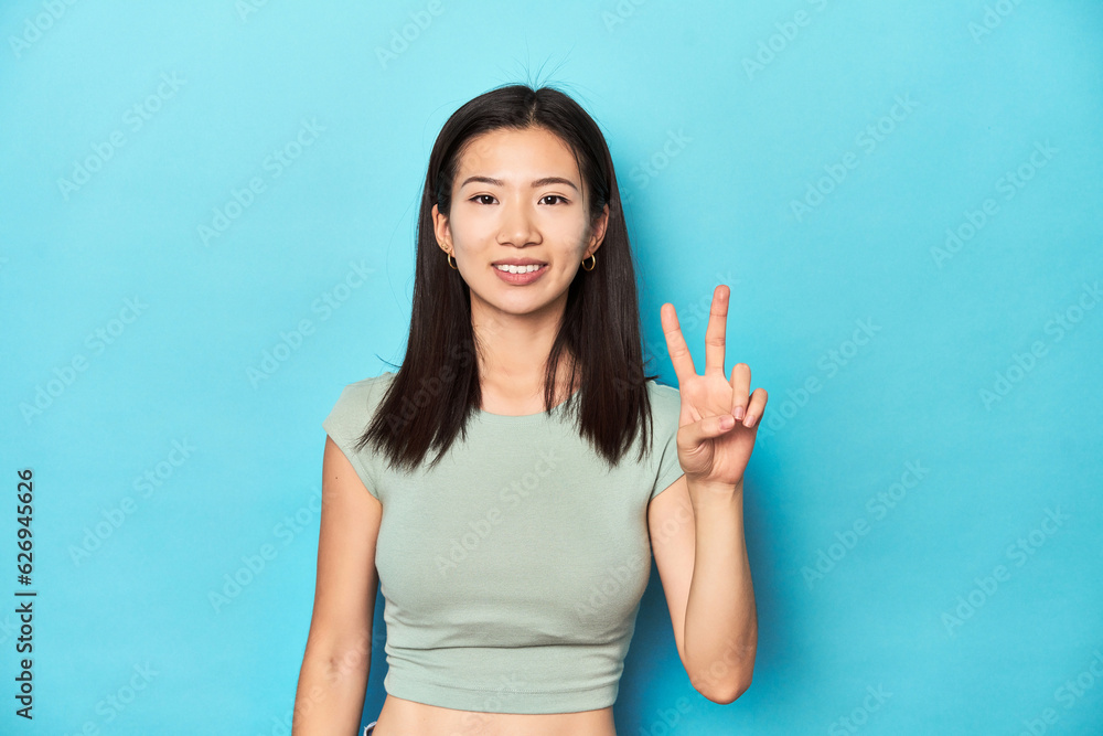 Asian woman in summer green top, studio backdrop, showing number two with fingers. Asian woman in summer green top, studio backdrop, showing number two with fingers.