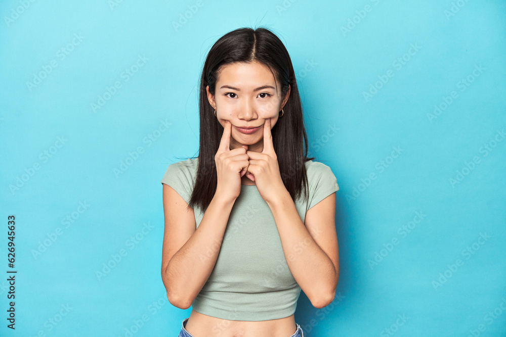 Asian woman in summer green top, studio backdrop, doubting between two options. Asian woman in summer green top, studio backdrop, doubting between two options.