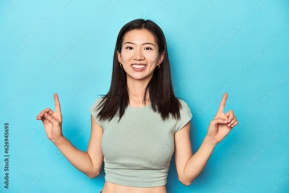 Asian woman in summer green top, studio backdrop, indicates with both fore fingers up showing a blank space. Asian woman in summer green top, studio backdrop, indicates with both fore fingers up showing a blank space.