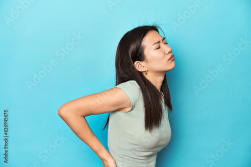 Asian woman in summer green top, studio backdrop, suffering a back pain.