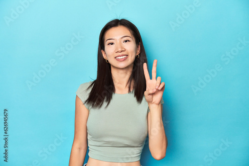 Asian woman in summer green top  studio backdrop  joyful and carefree showing a peace symbol with fingers.