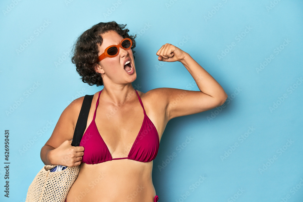 Young woman in bikini with beach bag raising fist after a victory, winner concept.