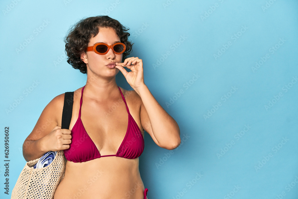 Young woman in bikini with beach bag with fingers on lips keeping a secret.