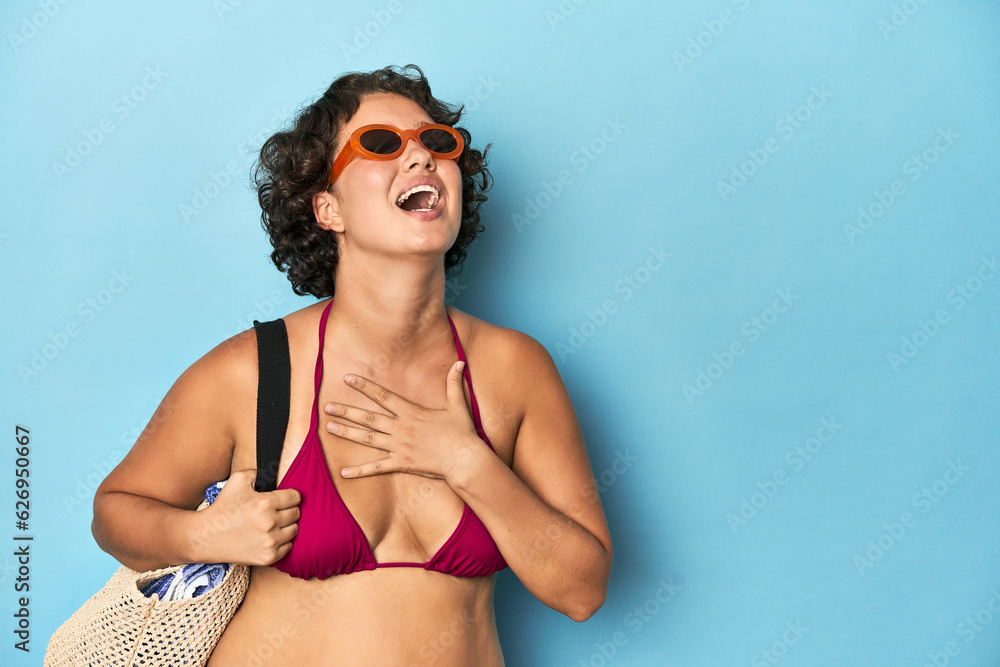 Young woman in bikini with beach bag laughs out loudly keeping hand on chest. Young woman in bikini with beach bag laughs out loudly keeping hand on chest.