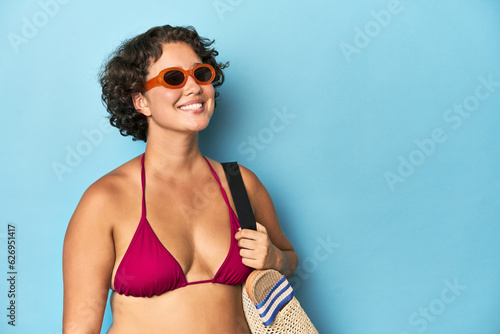 Young Caucasian woman in bikini holding a beach bag, studio shot. © Asier