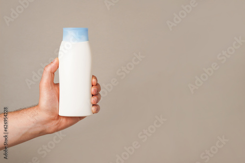 a man holding white bottle of lotion or shampoo in his hand, gray background with copy space