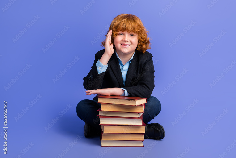 Full length photo of smart cheerful schoolkid sit floor pile stack book raise arm answer isolated on violet color background