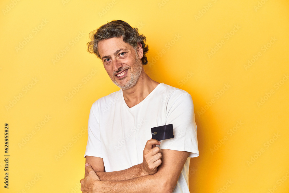 Man holding a credit card, yellow studio backdrop laughing and having fun. Man holding a credit card, yellow studio backdrop laughing and having fun.