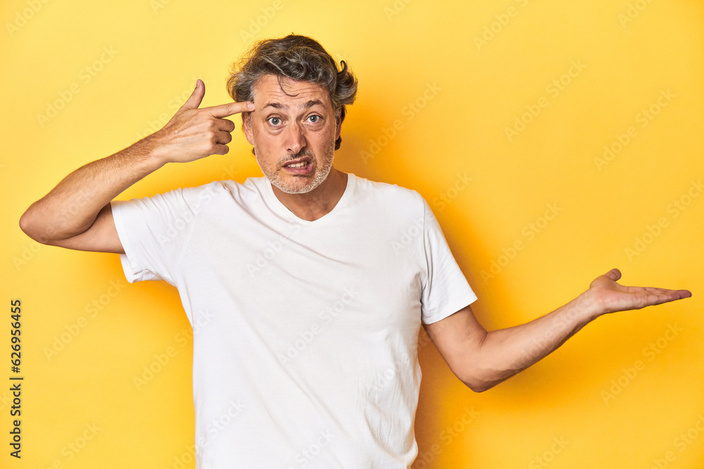 Middle-aged man posing on a yellow backdrop holding and showing a product on hand. Middle-aged man posing on a yellow backdrop holding and showing a product on hand.