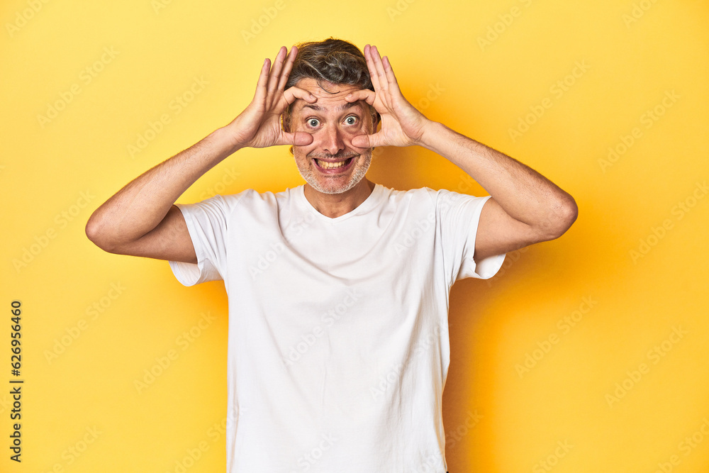 Middle-aged man posing on a yellow backdrop keeping eyes opened to find a success opportunity. Middle-aged man posing on a yellow backdrop keeping eyes opened to find a success opportunity.