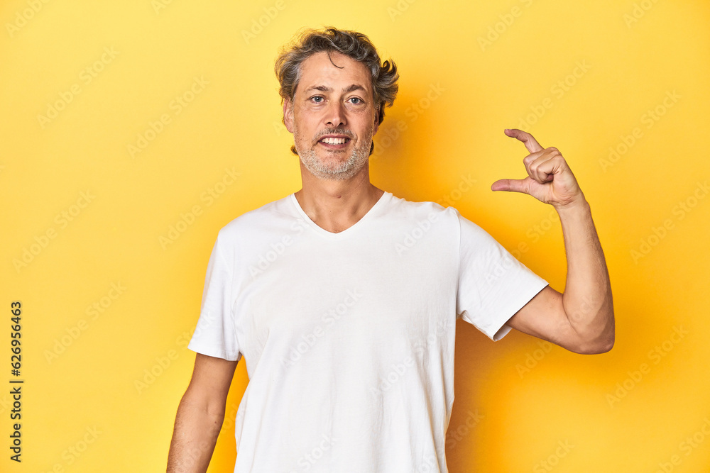 Middle-aged man posing on a yellow backdrop holding something little with forefingers, smiling and confident. Middle-aged man posing on a yellow backdrop holding something little with forefingers, smiling and confident.
