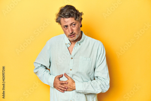 Middle-aged man posing on a yellow backdrop having a liver pain, stomach ache.