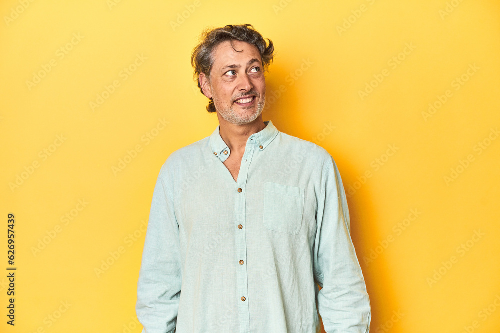 Middle-aged man posing on a yellow backdrop relaxed and happy laughing, neck stretched showing teeth.