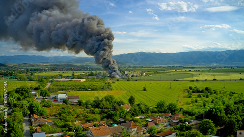A black column of smoke and a fire in a warehouse, against the backdrop of the city. Photo from above from a drone.