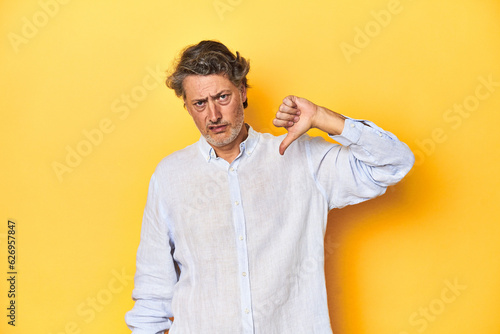Fototapet Middle-aged man posing on a yellow backdrop showing thumb down, disappointment concept