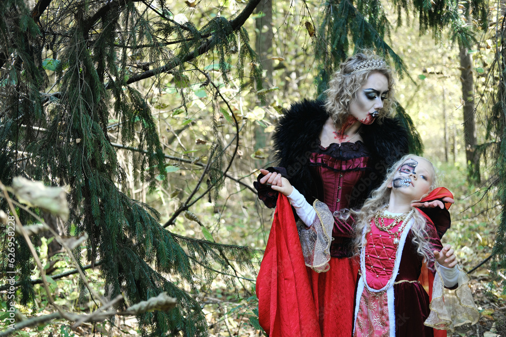A woman in the form of a vampire or a sorceress poses in the forest with a girl in fairy-tale makeup and medieval dress. Look for Halloween