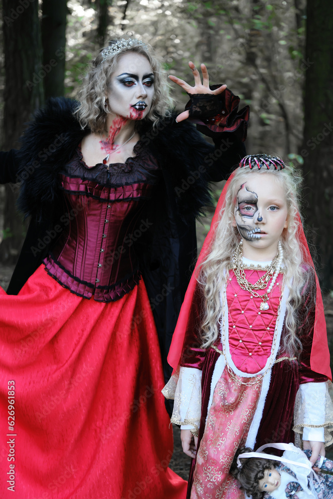 A woman in the form of a vampire or a sorceress is about to bite a princess girl in fairy-tale makeup and medieval dress. Look for Halloween. Mother and daughter