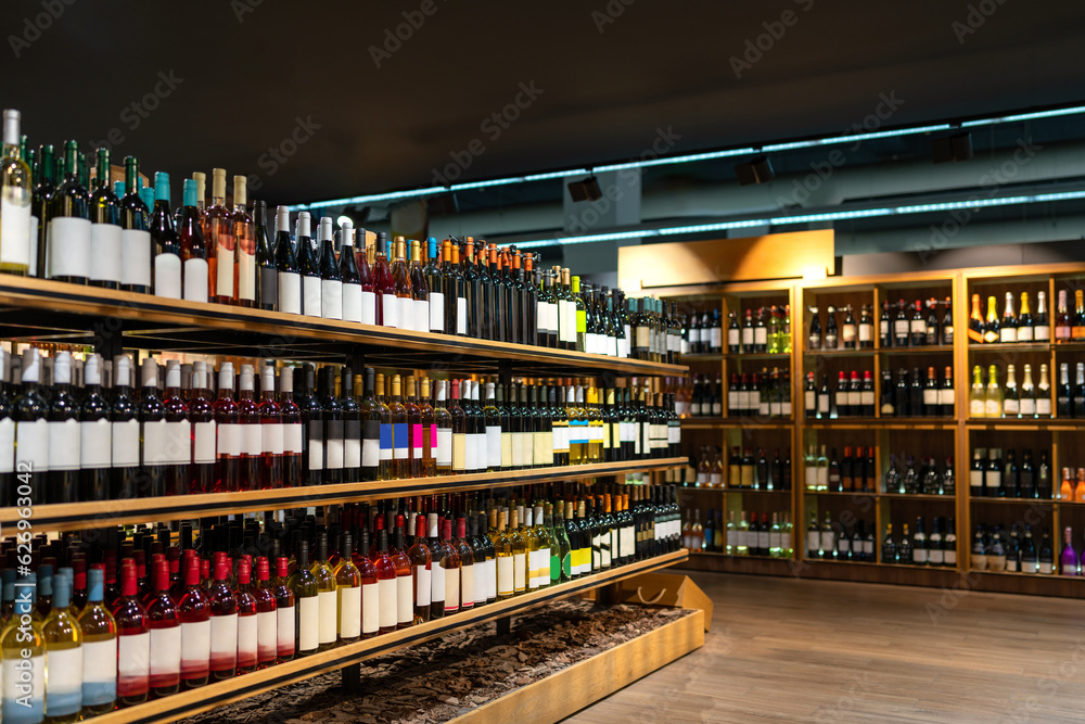 Wine bottles in a row on shelves in wine store, alcohol retail business.